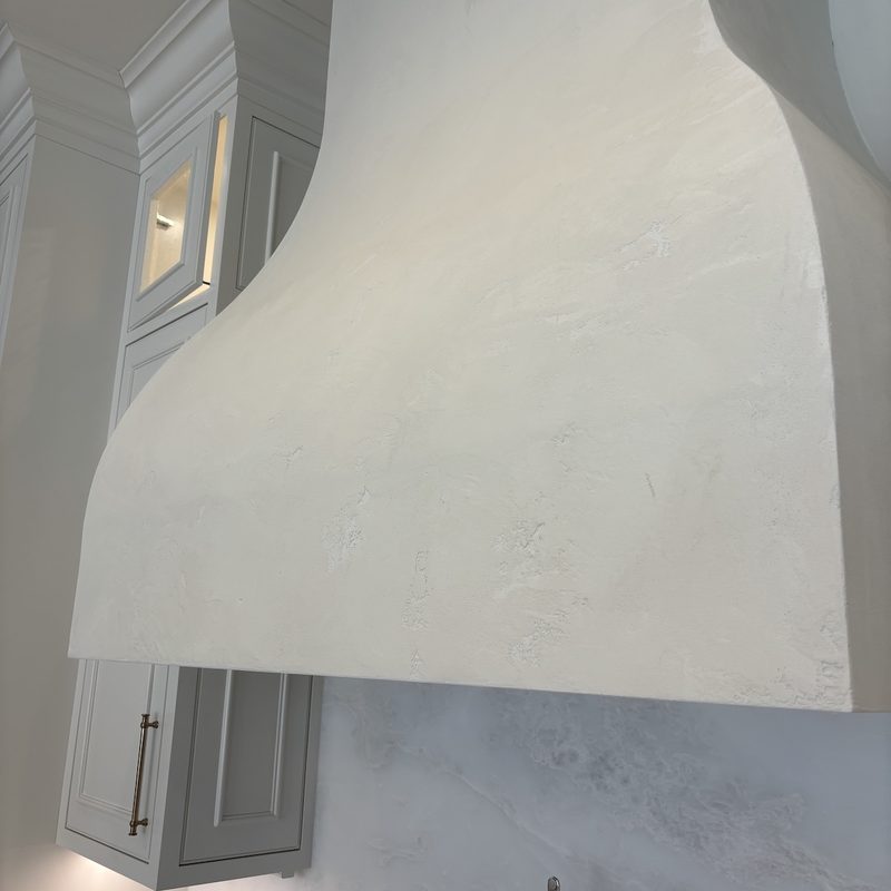Close view of the curved white range hood's textured, plaster-look surface
