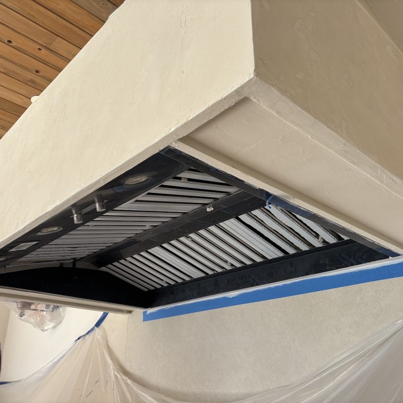 Underside of the cream range hood showing the vent insert, with blue tape along the edge