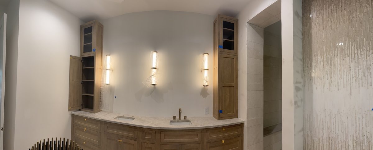 Panoramic view of the bathroom with a curved oak vanity, three sconces, and a stone mosaic feature wall at right