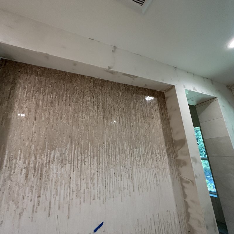 Looking up at a stone mosaic feature wall framed by a white surround with a mottled finish in progress