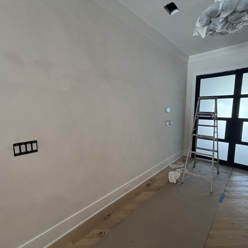 Long downstairs wall in a smooth, soft white finish, with a ladder by black-framed glass doors
