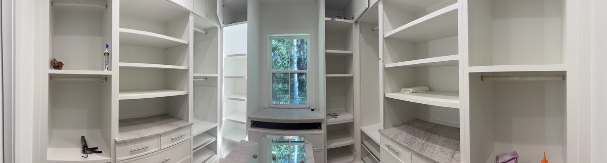 Panoramic view of a walk-in closet with white built-in shelving and a window at the far end