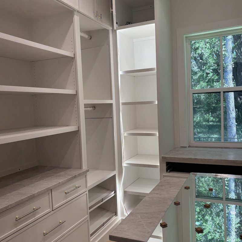 Walk-in closet with white shelves and drawers, a marble-look counter, and a window looking out to trees