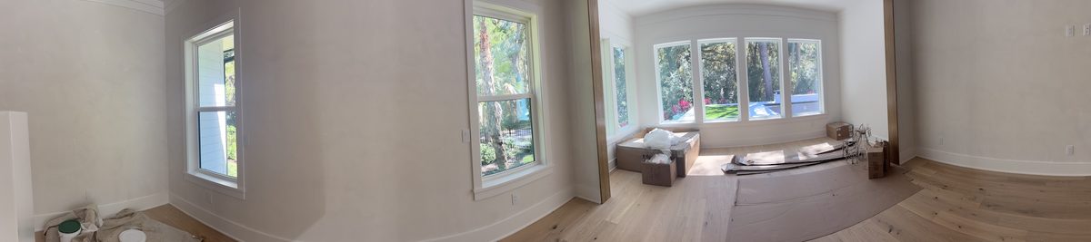 Panoramic view of a living room with soft white walls, large windows to the garden, and floors covered in protective paper